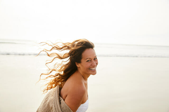 Portrait of a laughing mature woman with tousled long brown hair walking on a sandy beach in the late afternoon