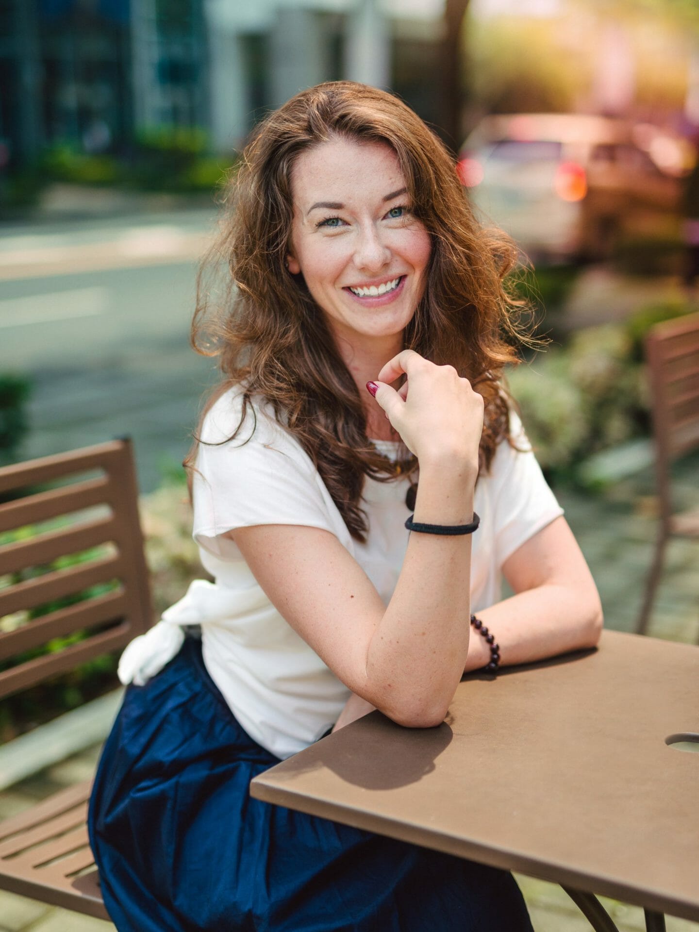 Woman with read hair sitting at a table outside smiling at the camera.